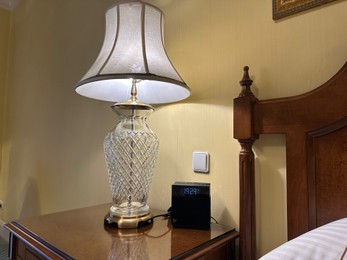 Photo of Lamp and electric clock on wooden bedside in luxury hotel