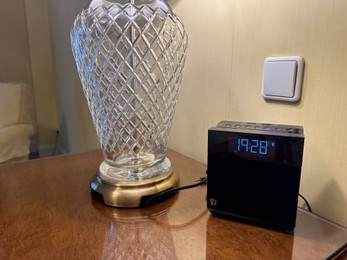 Photo of Lamp and electric clock on wooden bedside in luxury hotel