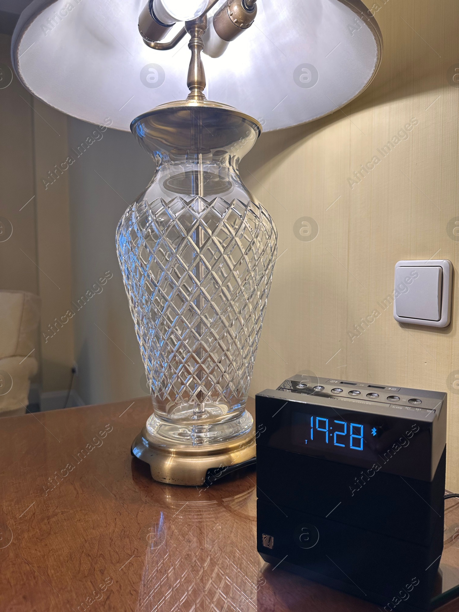 Photo of Lamp and electric clock on wooden bedside in luxury hotel