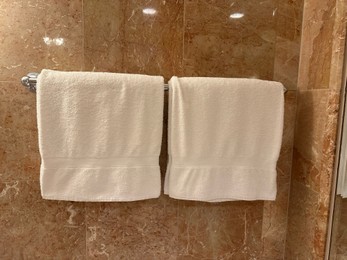 Photo of Soft terry towels hanging on tiled wall in hotel bathroom