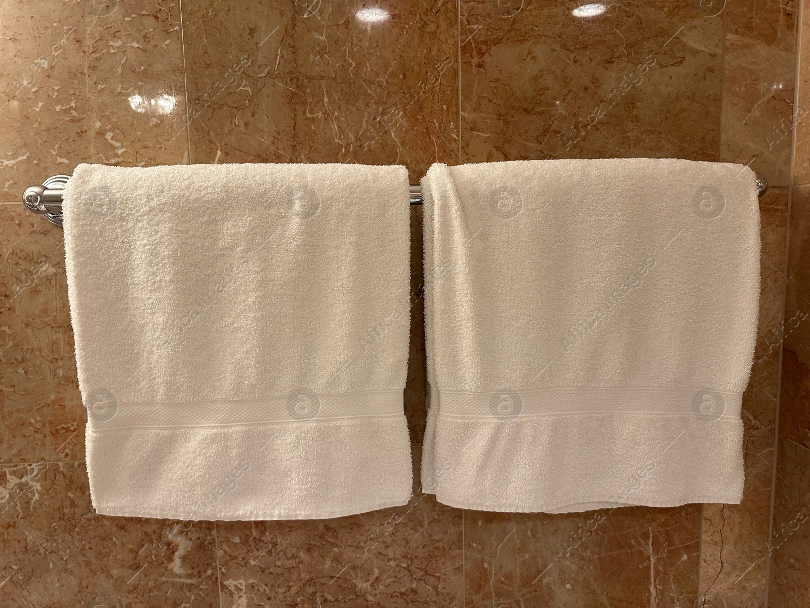 Photo of Soft terry towels hanging on tiled wall in hotel bathroom