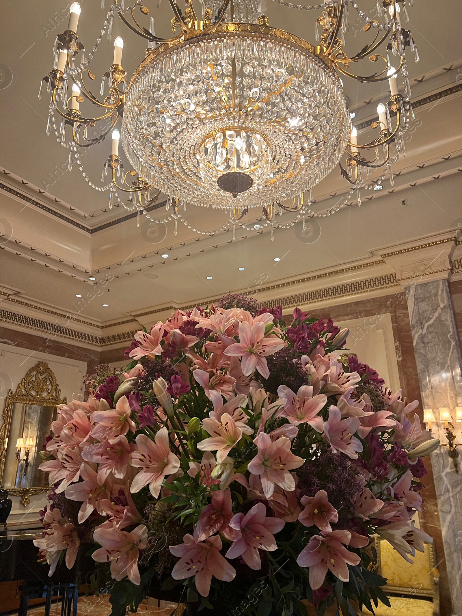 Photo of Luxury hotel interior. Beautiful bouquet of pink lilies and stylish chandelier in lobby