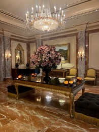 Photo of Luxury hotel interior. Beautiful bouquet on mirrored table and stylish chandelier in lobby