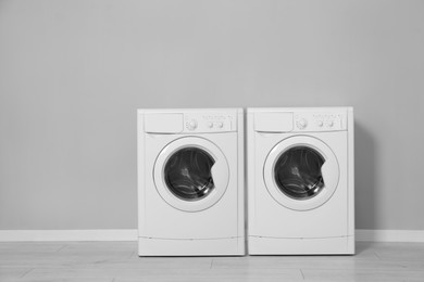 Two washing machines near grey wall in laundry room