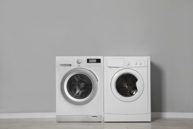 Two washing machines near grey wall in laundry room