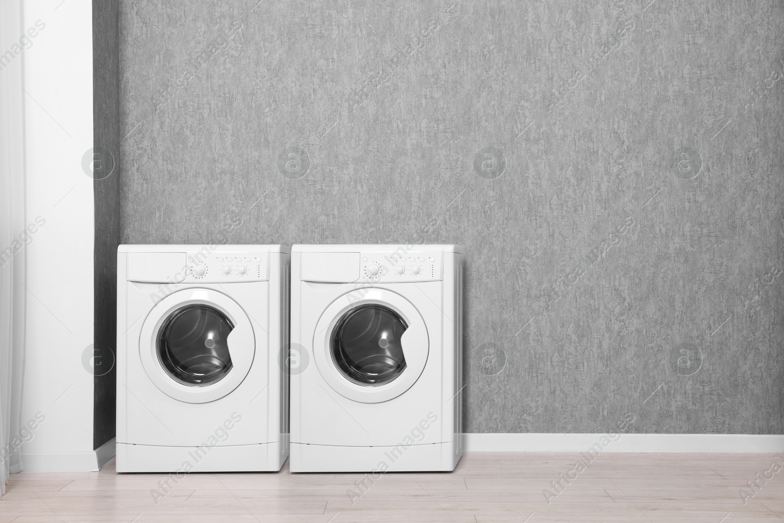 Image of Two washing machines near grey wall in laundry room