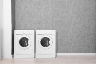 Two washing machines near grey wall in laundry room