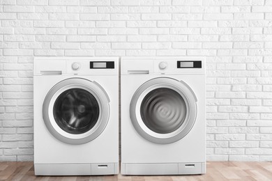 Two washing machines near white brick wall in laundry room