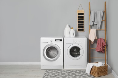 Two washing machines near grey wall in laundry room