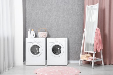 Two washing machines near grey wall in bathroom