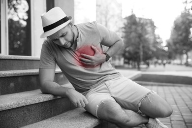 Image of Heart attack. Young man writhing in pain and pressing hand to chest on stairs outdoors