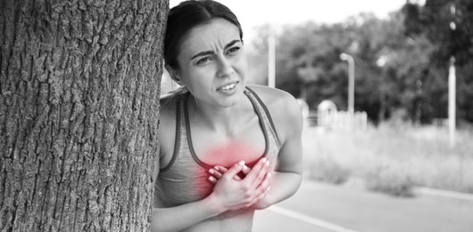 Image of Heart attack. Young woman suffering from pain in chest and leaning on tree outdoors. Banner design