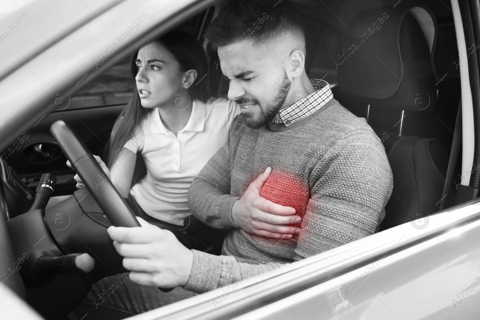 Image of Heart attack. Man suffering from pain in chest while driving, his worried girlfriend trying to stop car