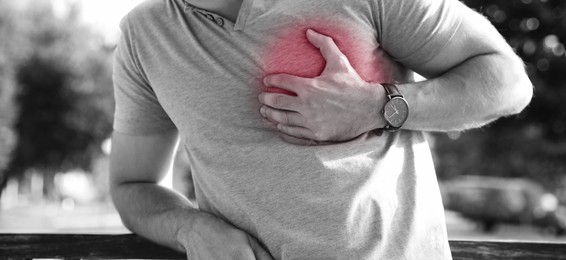 Heart attack. Man suffering from pain and pressing hand to chest outdoors, closeup