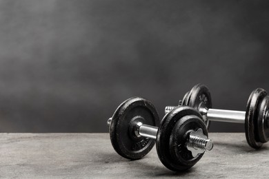 Two barbells on grey textured table, closeup. Space for text