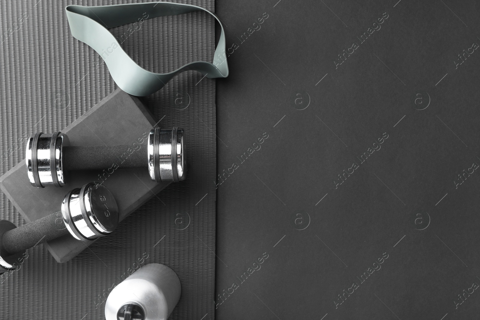 Photo of Dumbbells, yoga block, mat, thermo bottle and fitness elastic band on black background, flat lay. Space for text