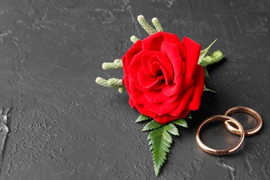 Photo of Stylish red boutonniere and rings on black table, space for text