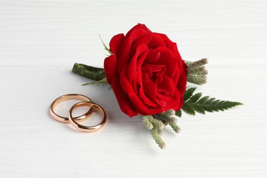Photo of Stylish red boutonniere and rings on white wooden table