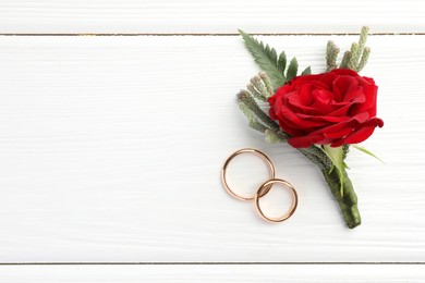 Photo of Stylish red boutonniere and rings on white wooden table, top view. Space for text