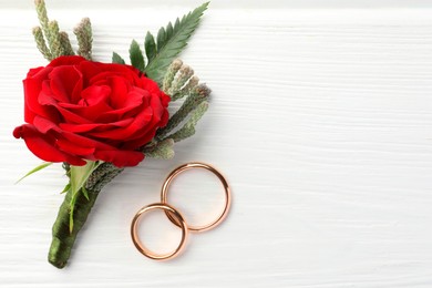 Photo of Stylish red boutonniere and rings on white wooden table, top view. Space for text