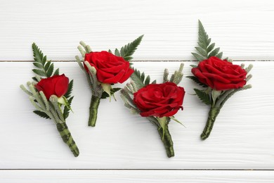 Photo of Many stylish red boutonnieres on white wooden table, flat lay