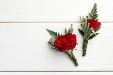 Photo of Two stylish red boutonnieres on white wooden table, top view. Space for text