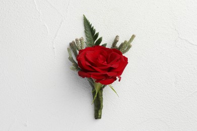 Photo of One stylish red boutonniere on white textured table, top view
