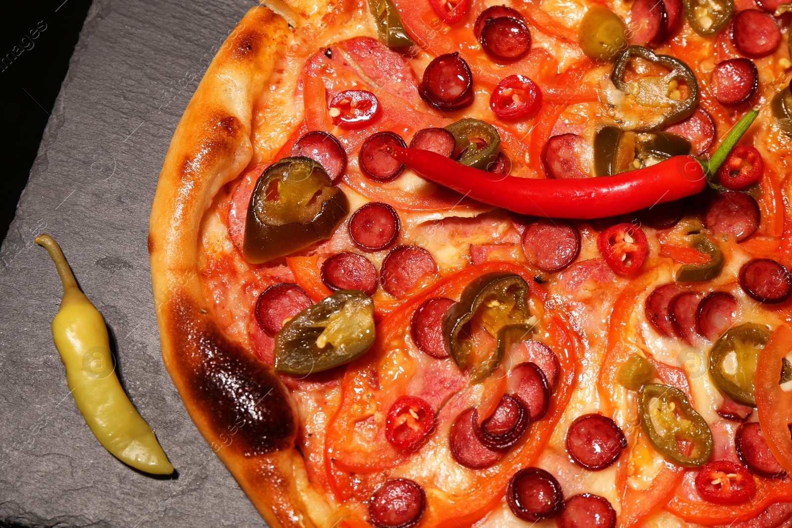 Photo of Delicious pizza Diablo and peppers on slate board against black background, top view