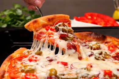 Photo of Woman taking piece of delicious pizza Diablo from baking tray, closeup