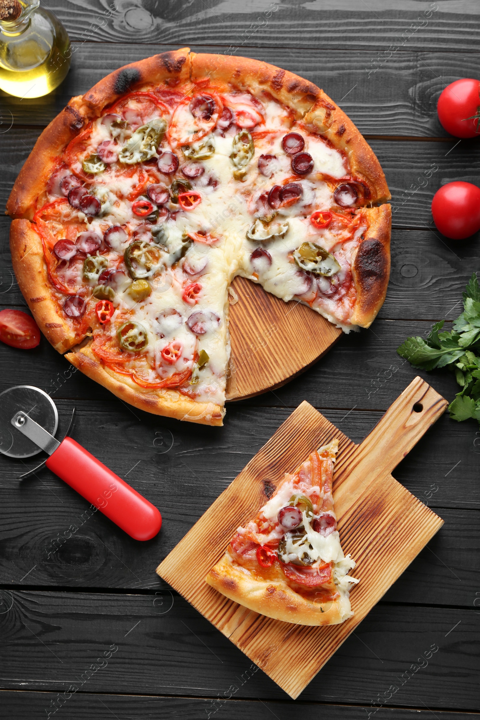 Photo of Delicious pizza Diablo, products and cutter on black wooden table, flat lay