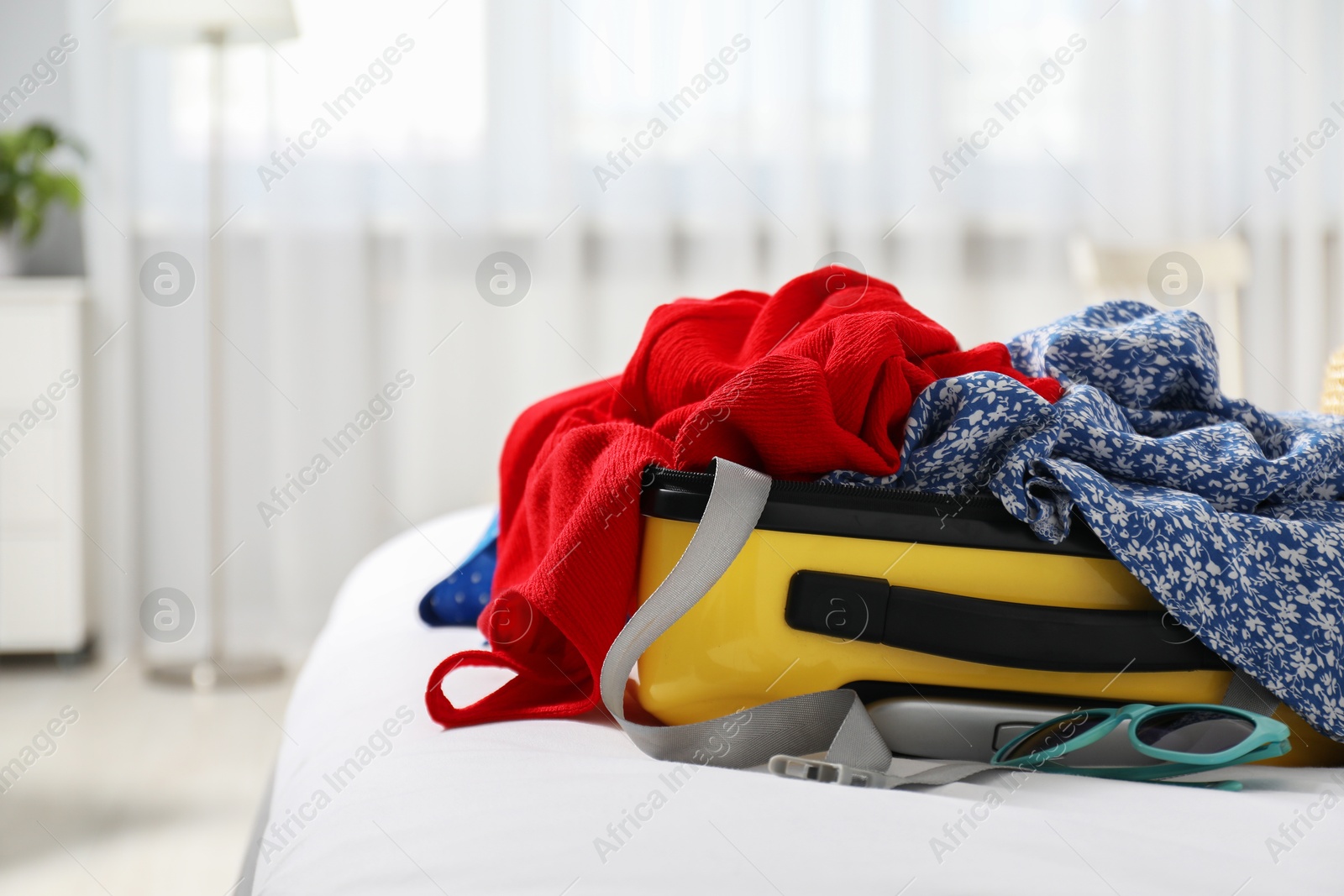 Photo of Open suitcase with traveler's belongings on bed, space for text