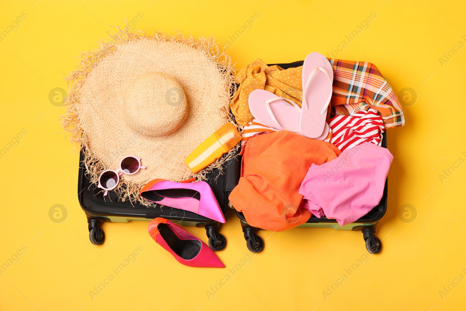 Photo of Open suitcase with traveler's belongings on yellow background, top view