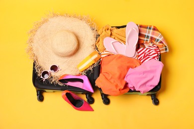 Open suitcase with traveler's belongings on yellow background, top view