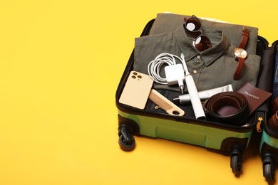 Open suitcase with traveler's belongings on yellow background, space for text