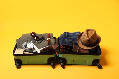 Photo of Open suitcase with traveler's belongings on yellow background