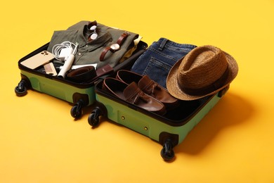 Open suitcase with traveler's belongings on yellow background