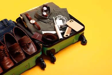 Photo of Open suitcase with traveler's belongings on yellow background