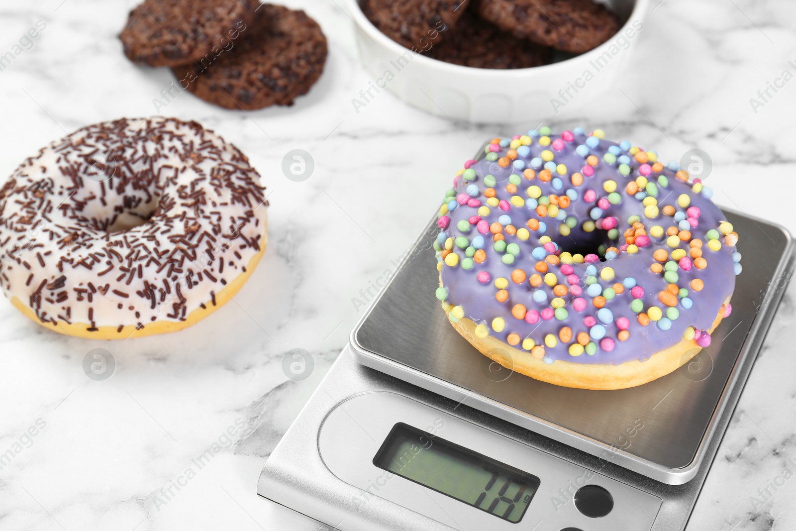 Photo of Kitchen scale with donut on white marble table, closeup