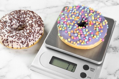 Photo of Kitchen scale with donut on white marble table, closeup