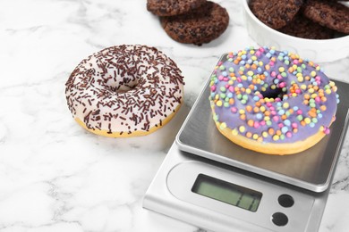 Photo of Kitchen scale with donut on white marble table, closeup. Space for text