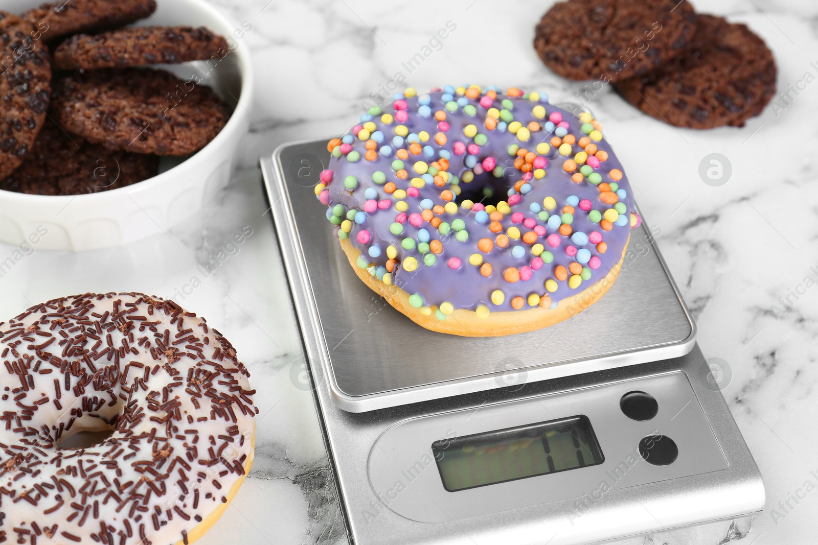 Photo of Kitchen scale with donut on white marble table, closeup