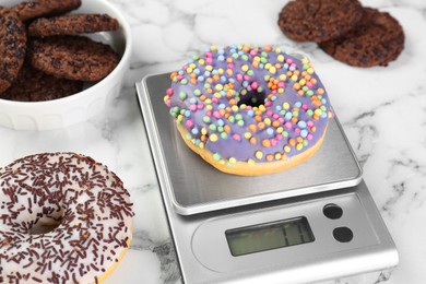 Kitchen scale with donut on white marble table, closeup