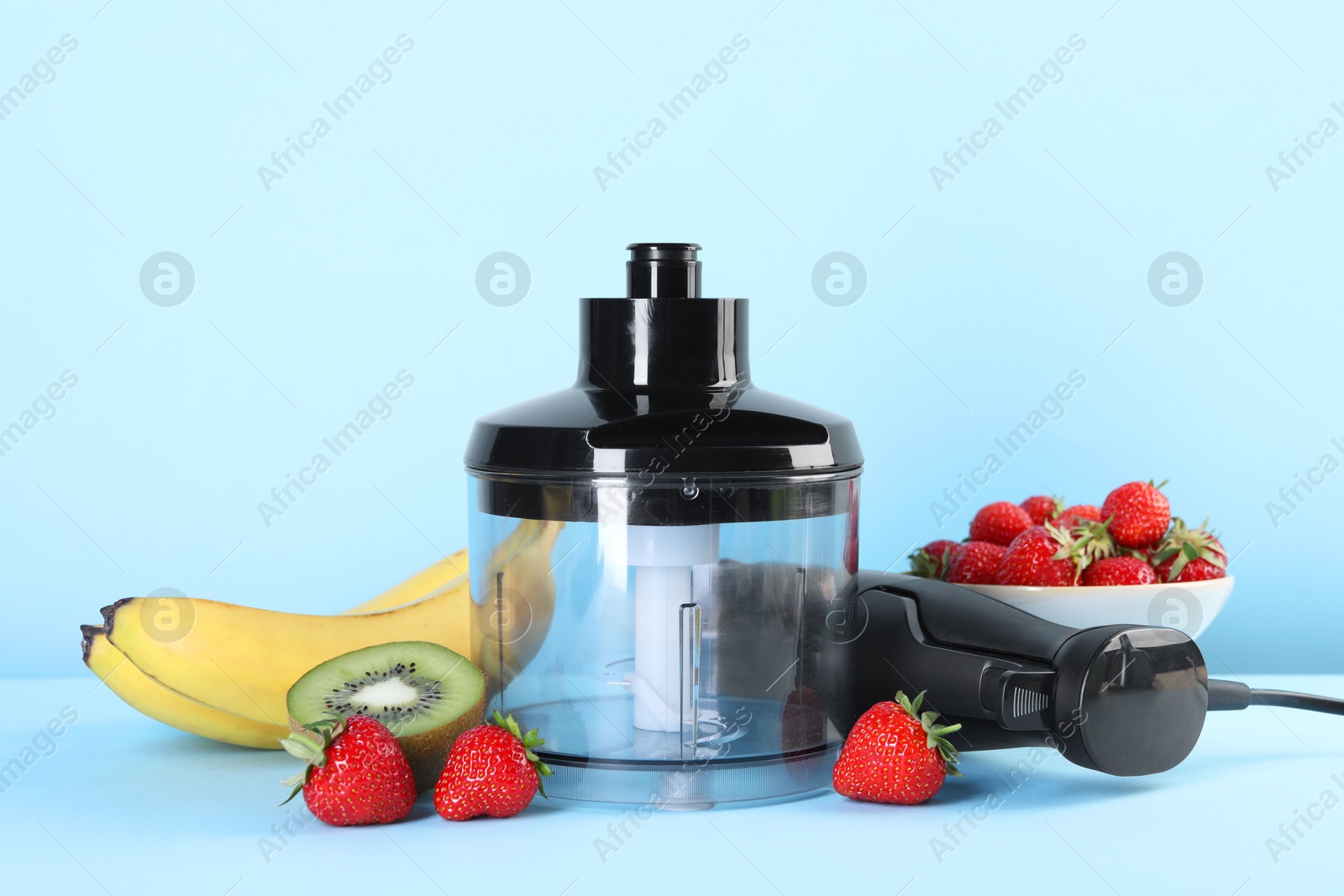 Photo of Hand blender kit, fresh fruits and strawberries on light blue background