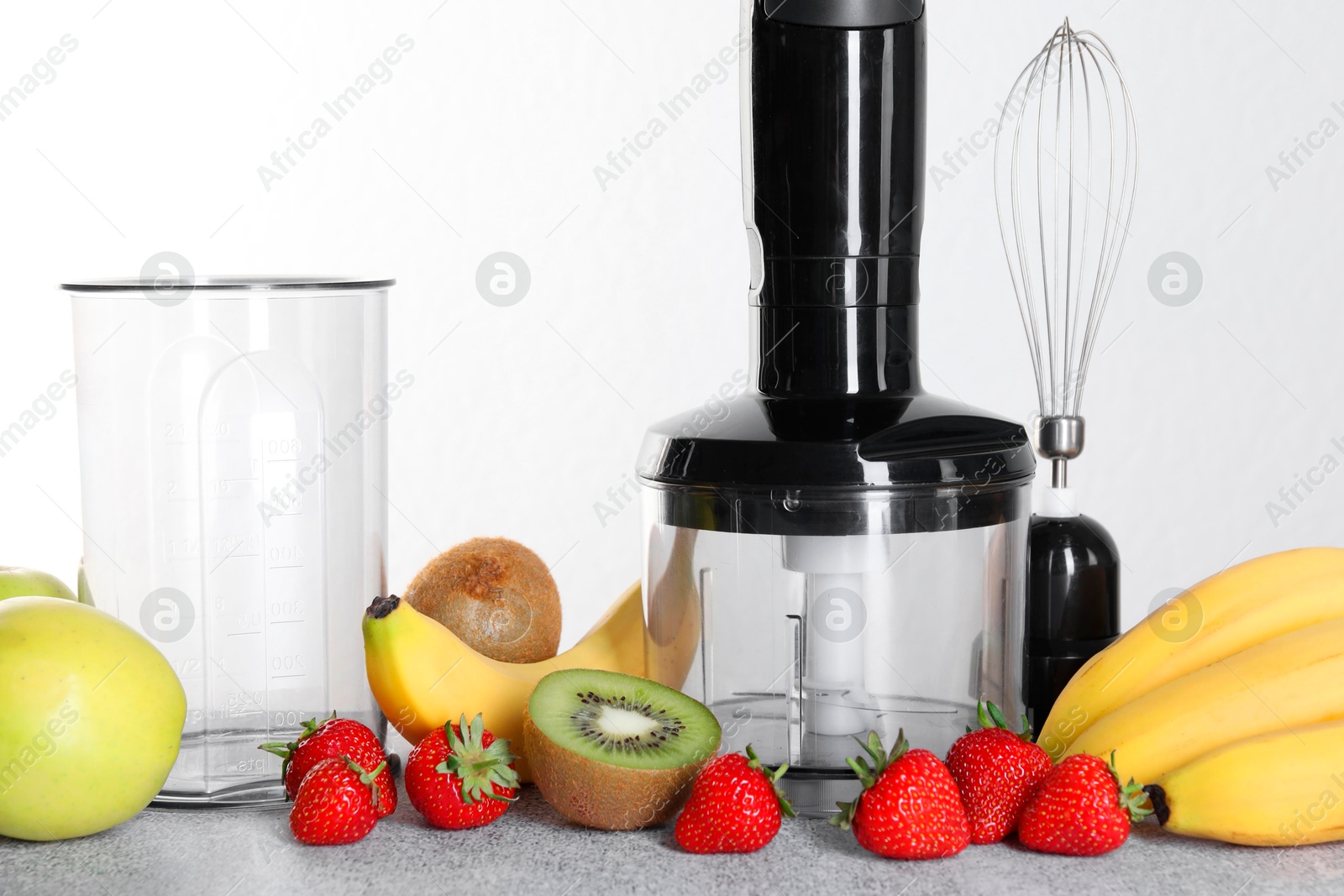 Photo of Hand blender kit, fresh fruits and strawberries on gray table against white background