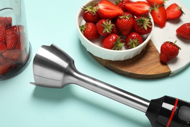 Photo of Hand blender kit and fresh strawberries on turquoise background, closeup