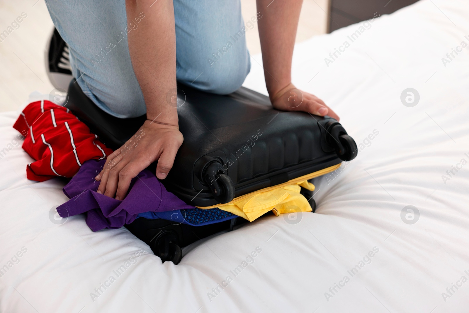 Photo of Man packing suitcase for trip on bed at home, closeup