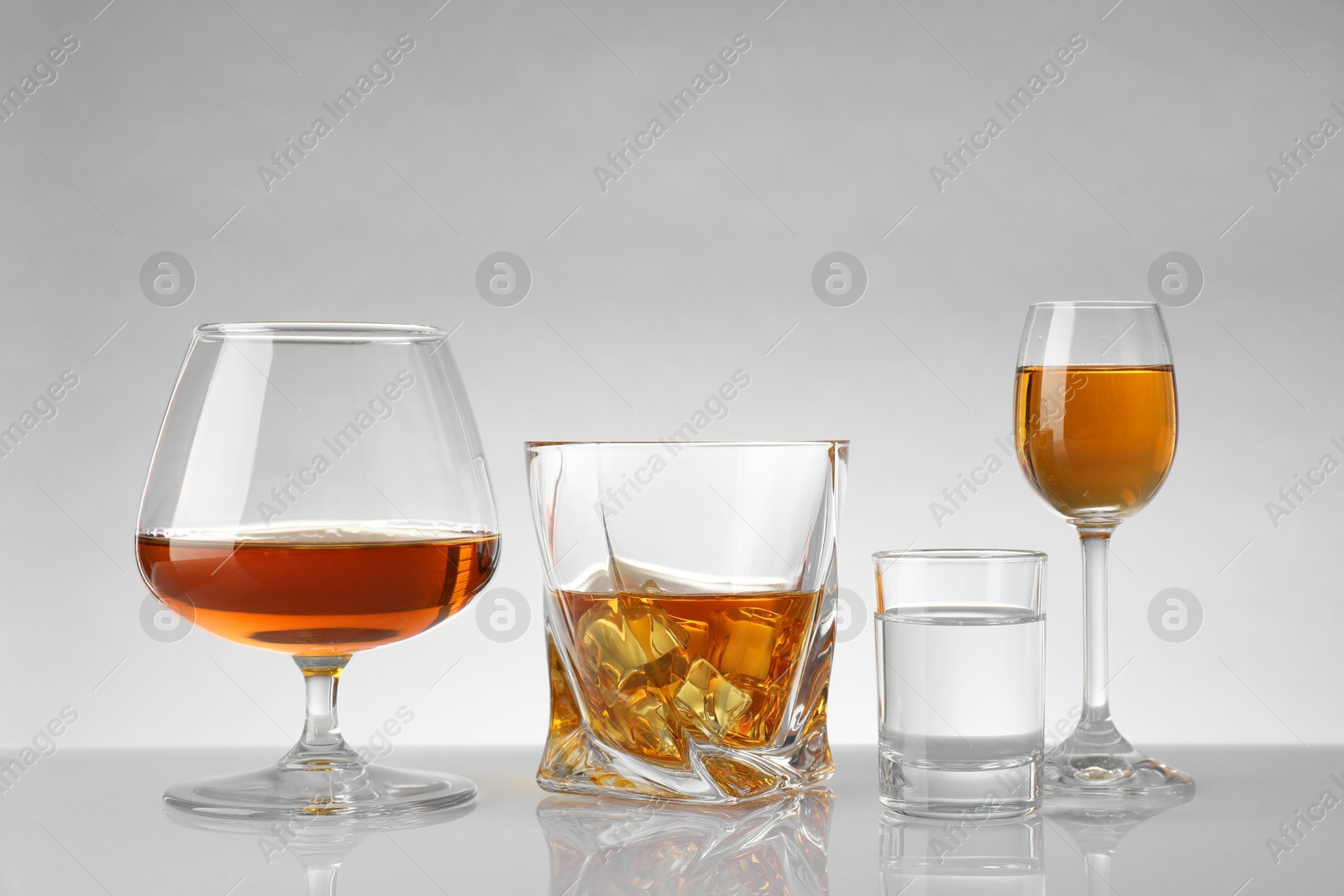 Photo of Glasses with different alcoholic drinks on white table against light background