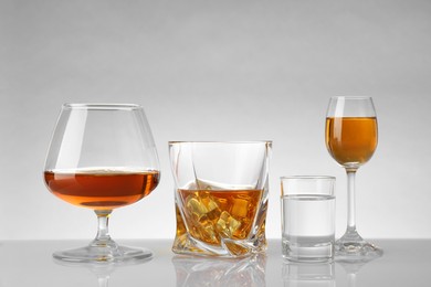 Glasses with different alcoholic drinks on white table against light background