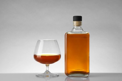 Photo of Bottle and glass with whiskey on white table against light background