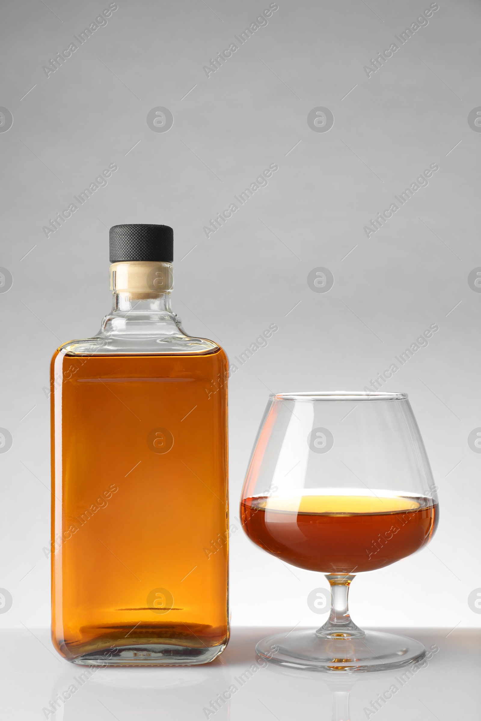 Photo of Bottle and glass with whiskey on white table against light background